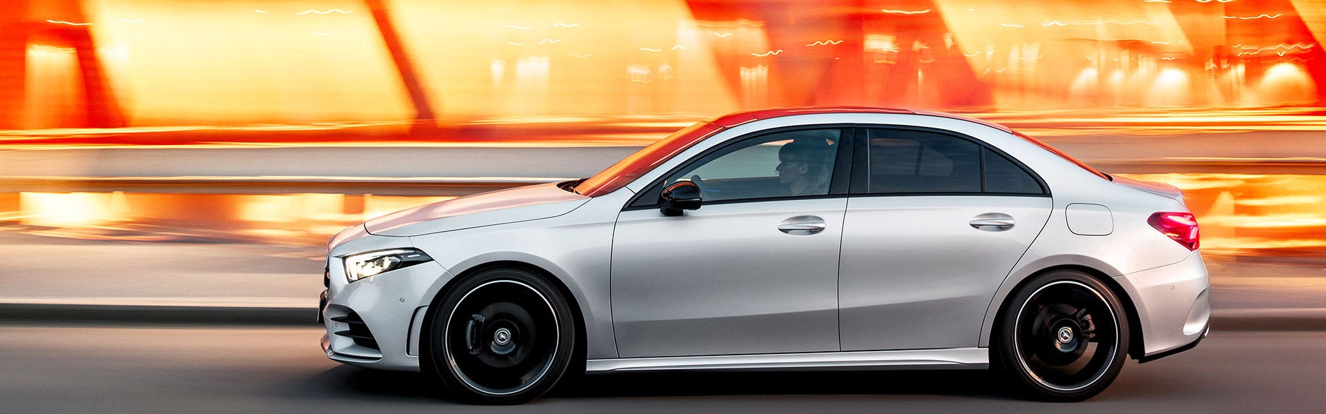 White Mercedes-Benz sedan driving at speed through a city at night, with motion blur and bright orange tunnel lights in the background.