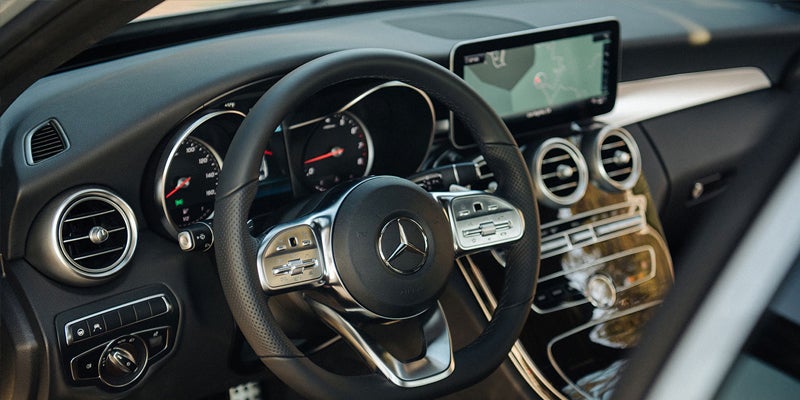 Interior view of a modern car's dashboard, showing the steering wheel with the Mercedes-Benz logo, digital display, and air vents.