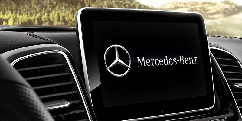 An in-car display screen shows the Mercedes-Benz logo and name. Air vents and dashboard trim are visible.