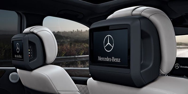 Rear passenger seat with a headrest screen displaying the Mercedes-Benz logo. Another headrest screen is visible in the background.
