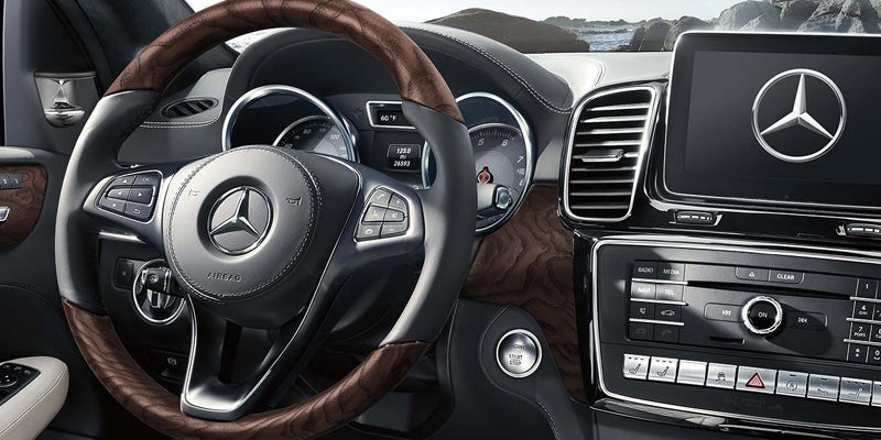 Interior view of a Mercedes-Benz dashboard and steering wheel, featuring a wood-trimmed steering wheel and infotainment screen.