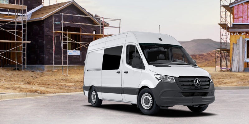 A white Mercedes cargo van on a paved street at a construction site with two partially built houses in the background.