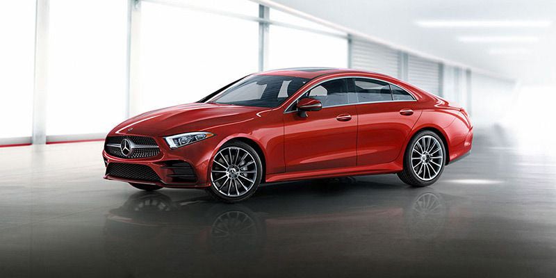 Red luxury sedan positioned diagonally in a bright, modern showroom setting.