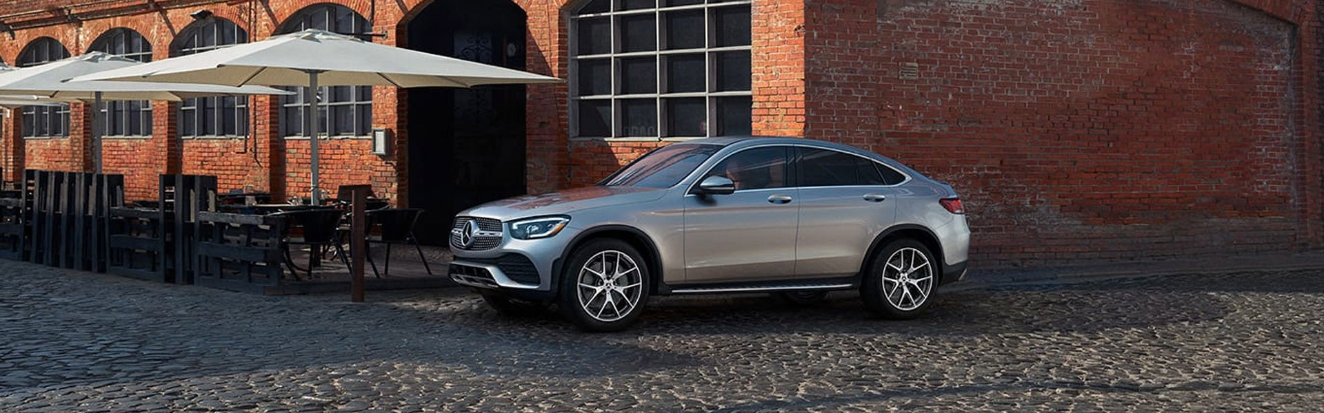 Silver Mercedes-Benz SUV coupe parked on cobblestone beside a brick building