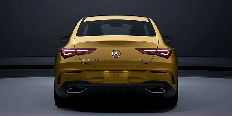 Rear view of a gold Mercedes-Benz sedan showing taillights and logo.