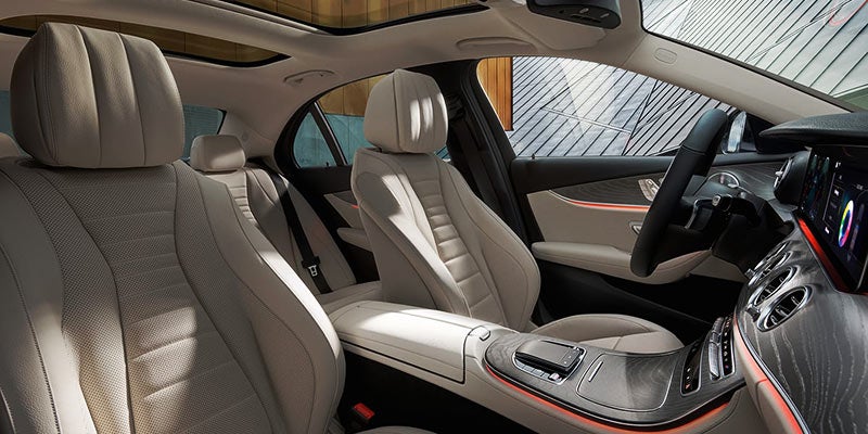 Interior of a luxury car with light colored seats, dashboard with digital display, and sunroof.