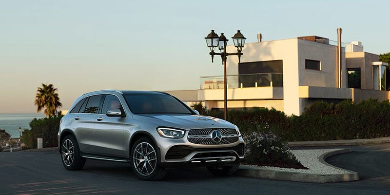 Silver Mercedes-Benz GLC 300 SUV on a winding road with a modern white house and palm trees.