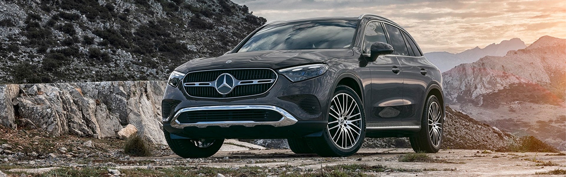 A black Mercedes-Benz GLC SUV parked on a rocky path against a backdrop of mountains at sunset.