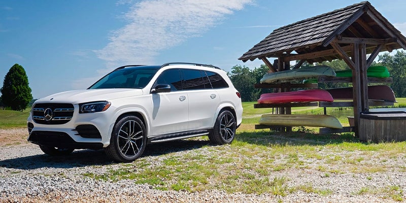 White Mercedes-Benz SUV parked on grass near a wooden structure