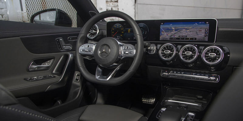 The interior of a car shows a black steering wheel with a Mercedes-Benz logo, dashboard displays, and side door details.