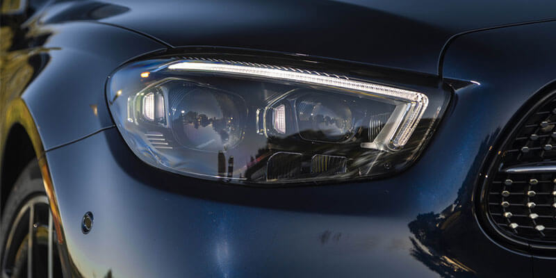 Close-up of a blue car's headlight, featuring a bright LED strip and a parking sensor below.
