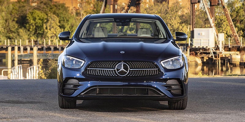 Front view of a dark blue Mercedes-Benz E-Class sedan with a large grille and headlights, parked outdoors.