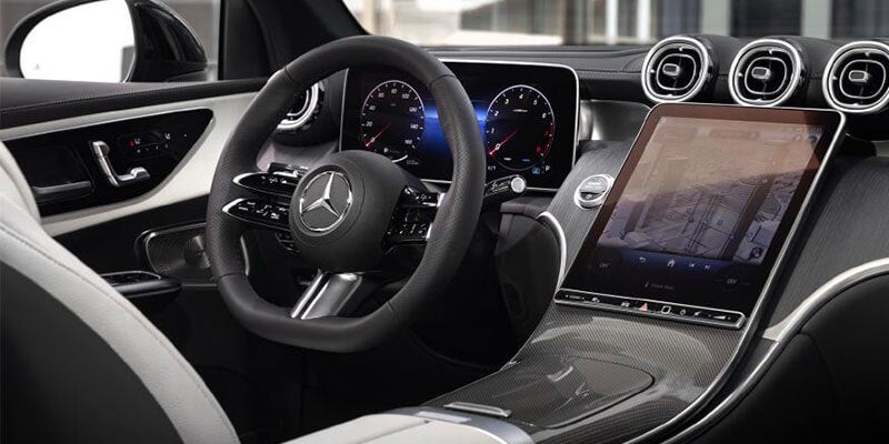 Interior of a Mercedes-Benz car, showing a steering wheel, digital dashboard, and a large central touchscreen.