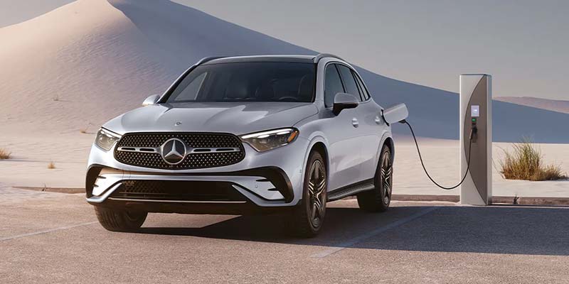A silver Mercedes-Benz electric vehicle is charging at a station in a desert landscape.