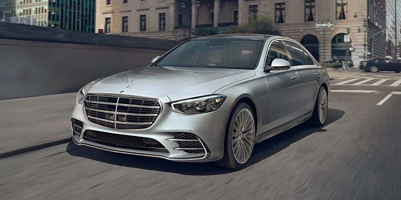 A luxury silver sedan driving down a city street