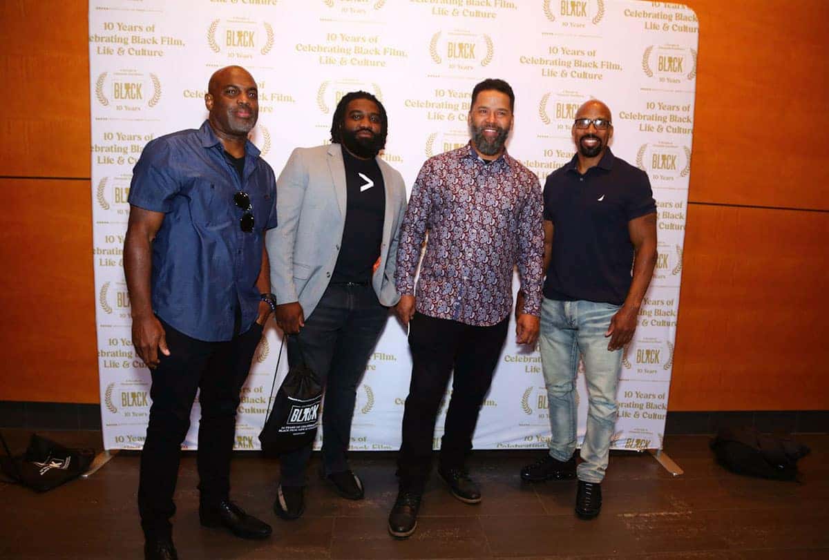 Attendees at an event sit in rows of white folding chairs in a museum with vehicles and art displays.