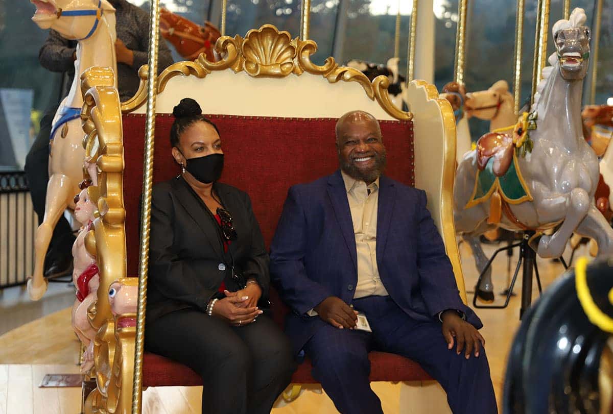 A Black woman smiles at a booth for the Greater Cleveland Urban Film Festival, displaying Celebrating Black apparel and sneakers.