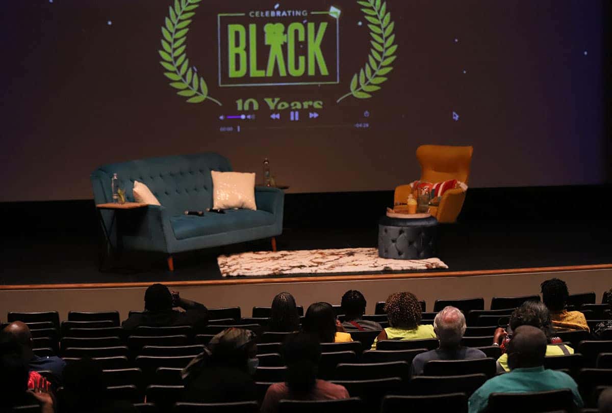 A stage is set like a living room with a blue couch and an orange armchair. A screen shows Celebrating Black 10 Years.