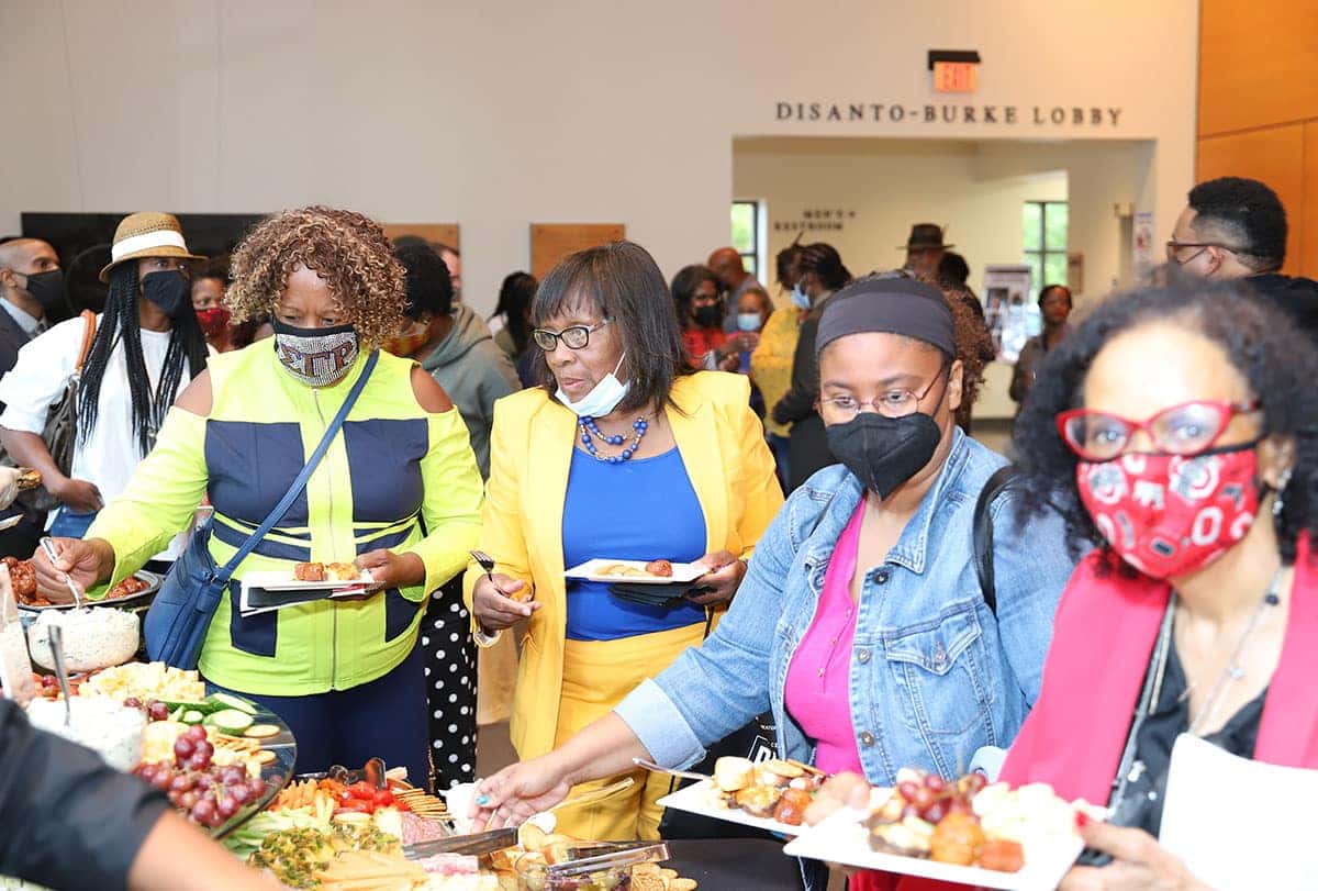 Four men of color stand side-by-side, smiling in front of a white backdrop with repeated text.