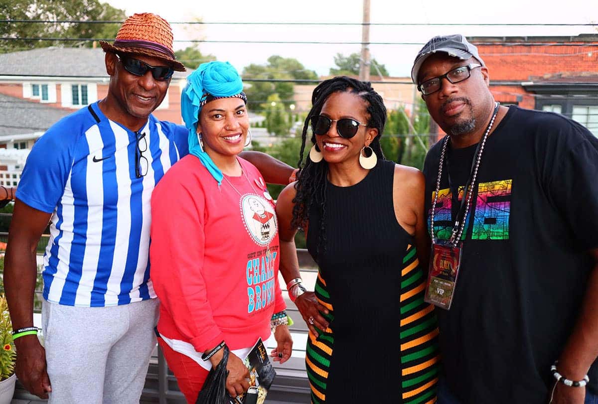 Four smiling Black adults, two men and two women, pose closely for a photo.