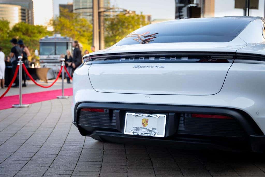 Rear view of a white Porsche Taycan 4S. A red carpet and attendees are visible in the background.