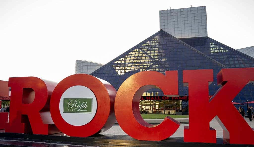 Large red letters ROCK in the foreground, with the Rock & Roll Hall of Fame building in the background.