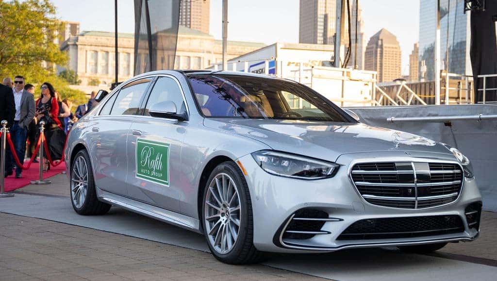 A silver Mercedes-Benz sedan with a green Rafih Auto Group decal parked on pavement next to a red carpet.
