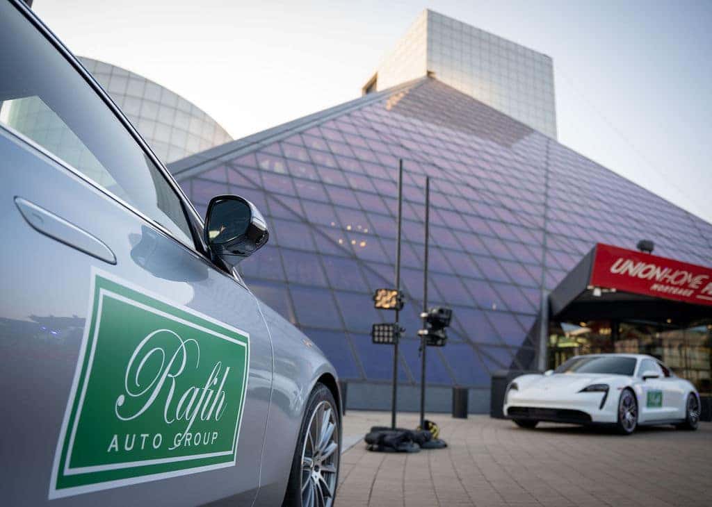 Gray car with Rafih Auto Group logo in foreground, large glass building, and white car in background.
