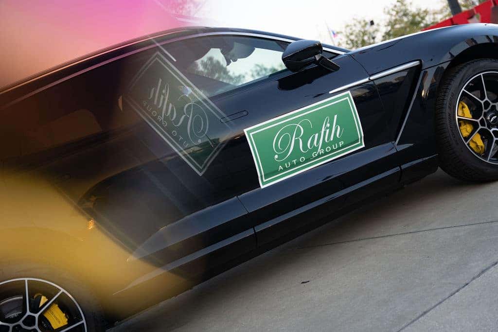 Side view of a glossy black car with a green Rafih Auto Group sign on the door.