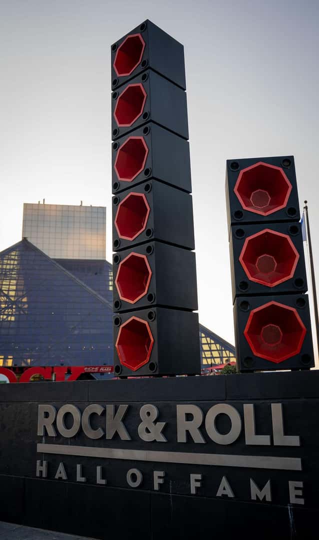 The Rock & Roll Hall of Fame sign with large speaker stacks, pyramids, and a glass-paneled building in the background.