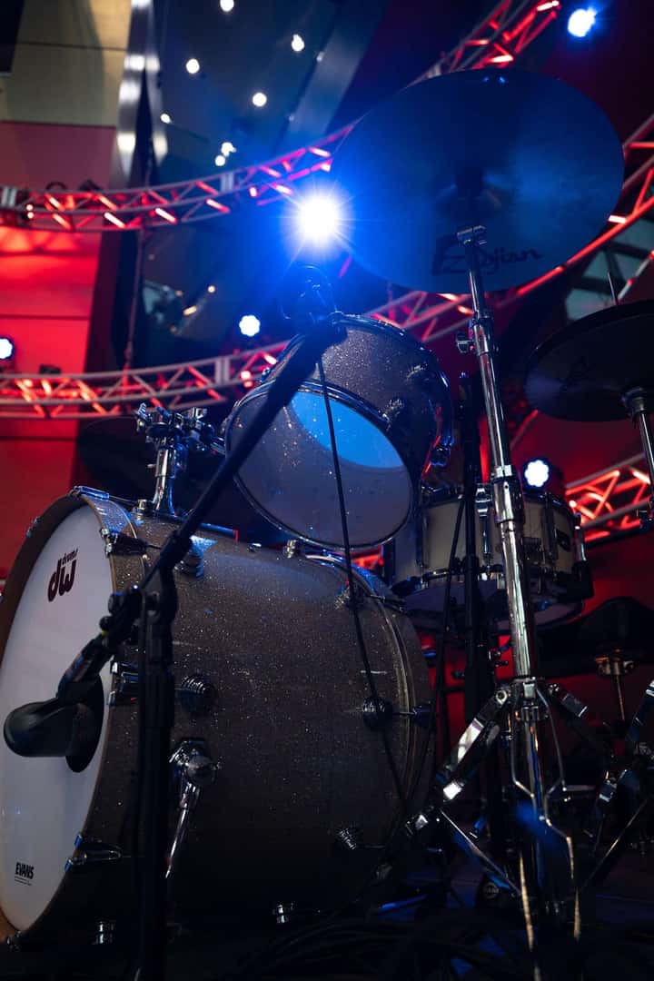 A glittery drum kit under blue and red stage lights, with a bright blue spotlight on a cymbal.