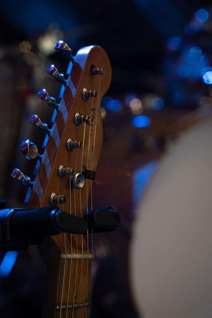The headstock of a guitar with tuning pegs and strings. Blue bokeh lights are visible in the blurry background.