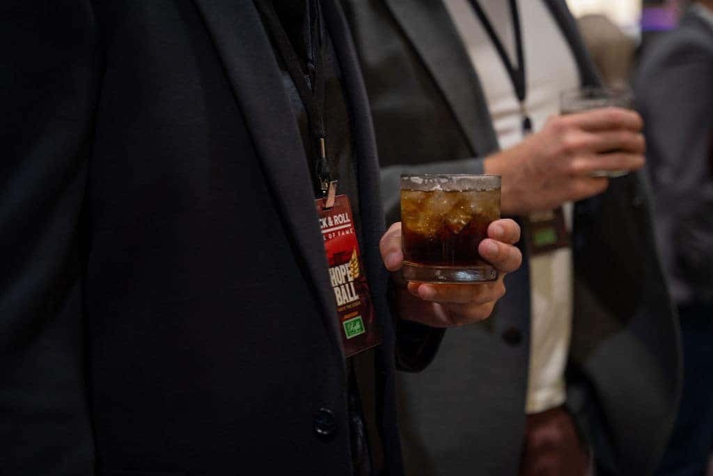 A spacious event hall with a glass atrium ceiling, black tables with red floral centerpieces, a DJ booth, and Hope Ball signage.