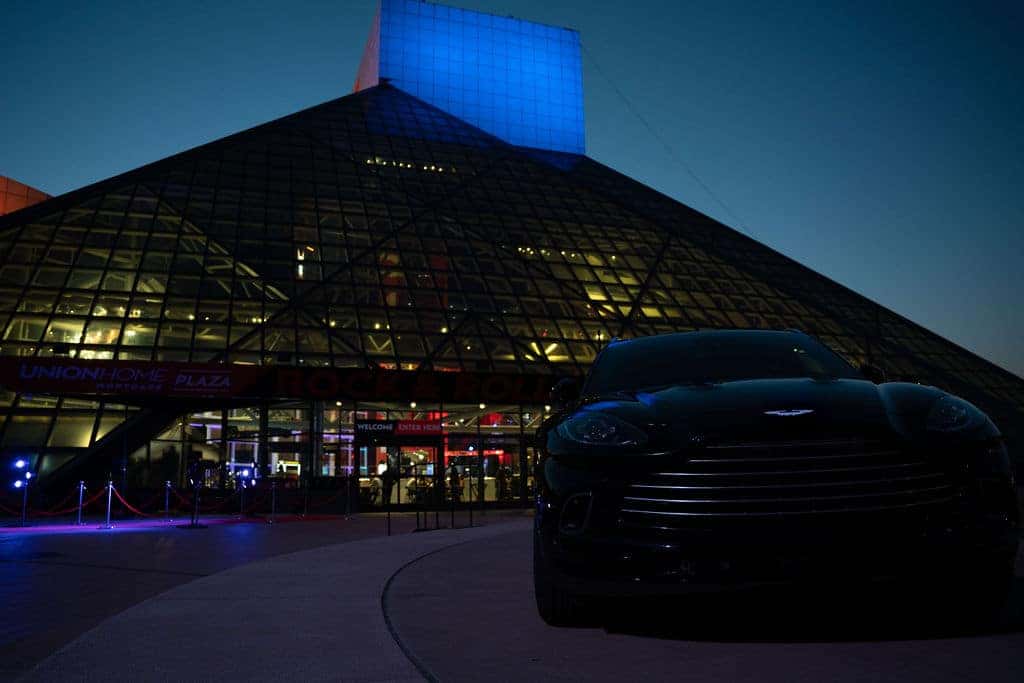 Front view of a shiny gray Mercedes-Benz with a prominent grille and hood ornament, illuminated by bright lights.