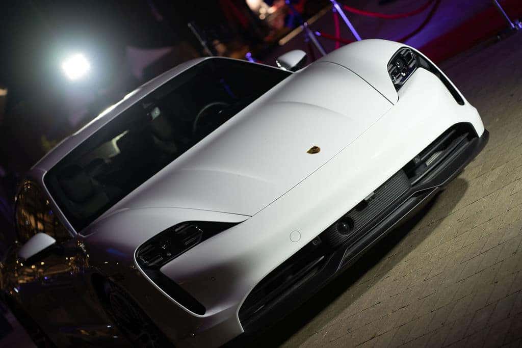 Front view of a white Porsche sports car angled low, with bright lights reflecting on its hood.