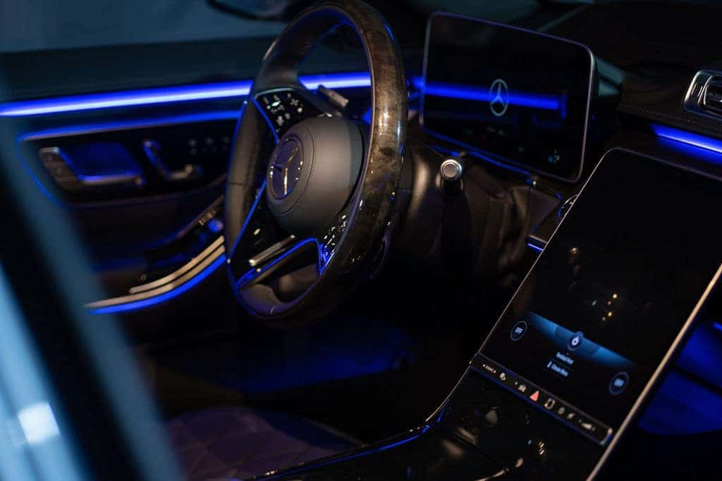 Dark car interior featuring a steering wheel on a black dashboard with blue ambient lighting.