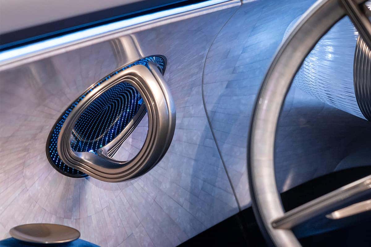 Close-up of a futuristic car interior showing a metallic circular speaker and part of the steering wheel.