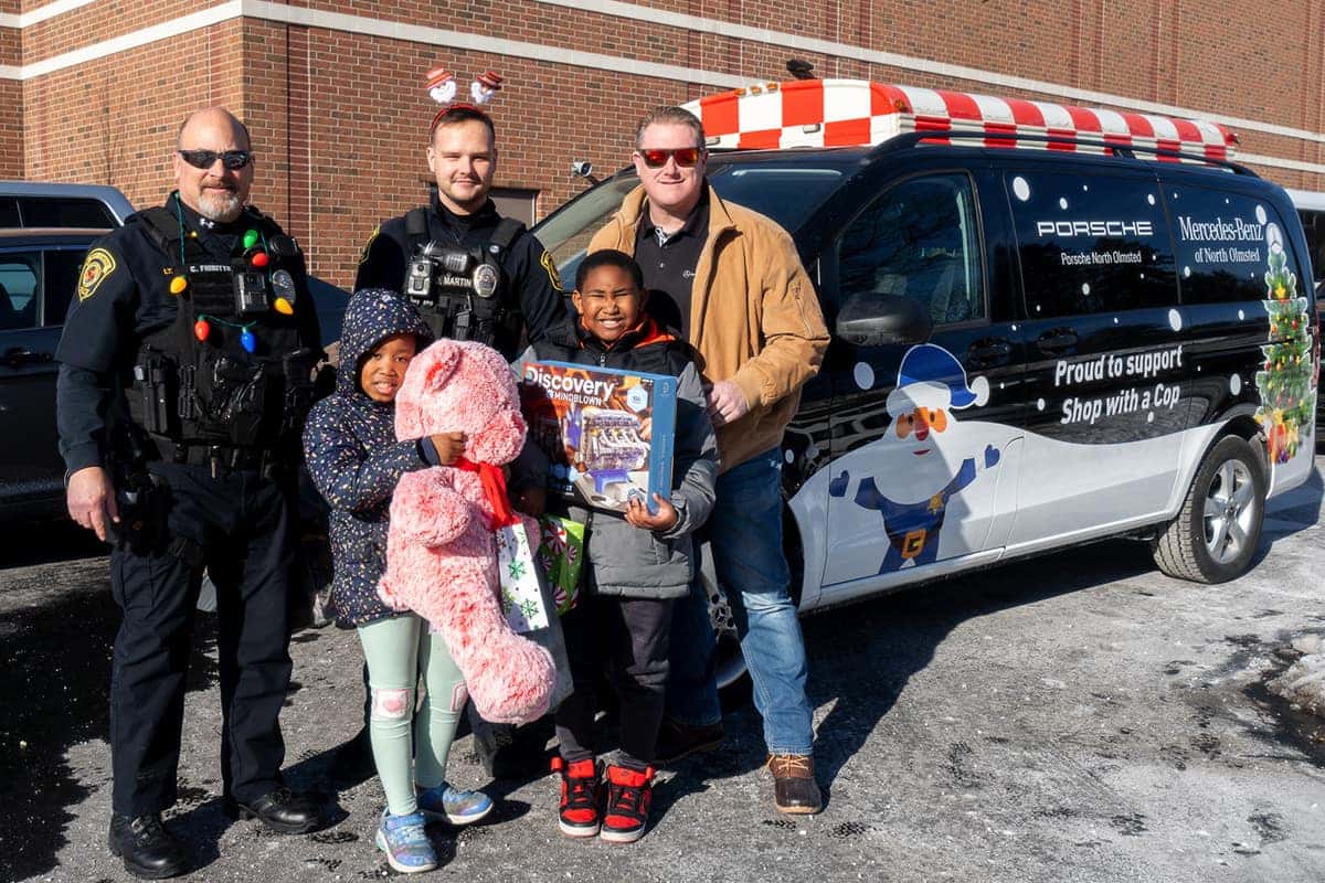 Two security officers, one pushing a cart, stand near a man holding Christmas headbands in a crowded Walmart.