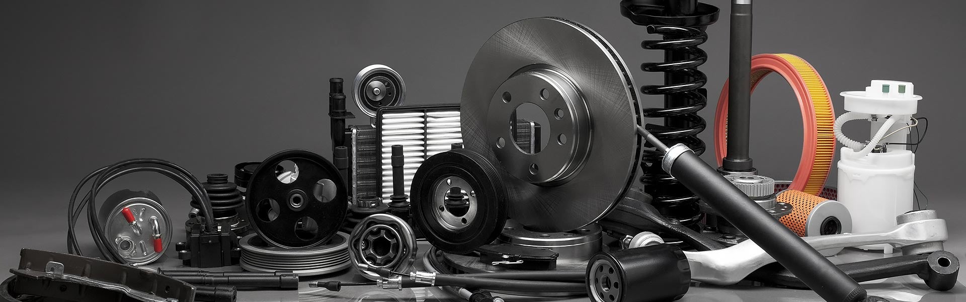 A collection of automotive parts arranged together, including brake rotors, shock absorbers, suspension springs, filters, belts, pulleys, and various engine and mechanical components displayed against a neutral background.
