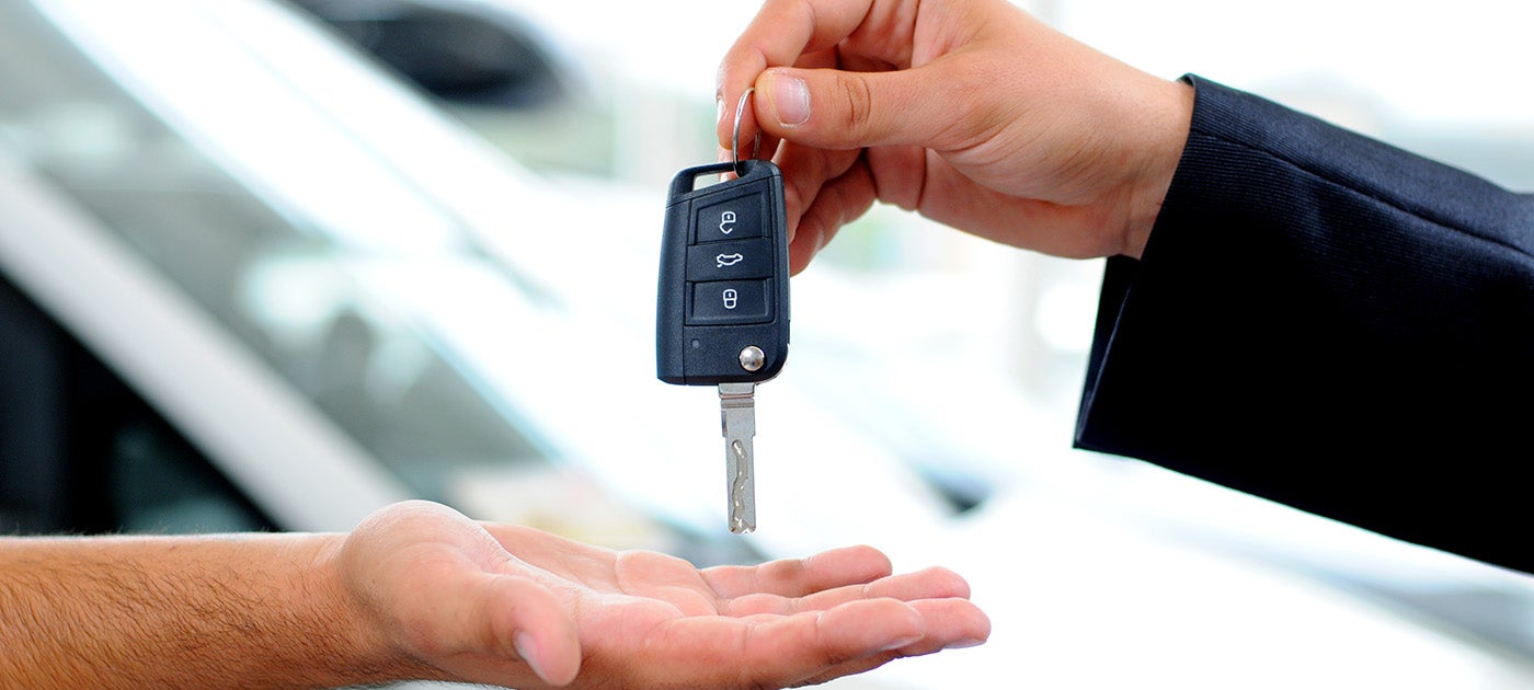 A person in a suit hands over car keys to another individual.