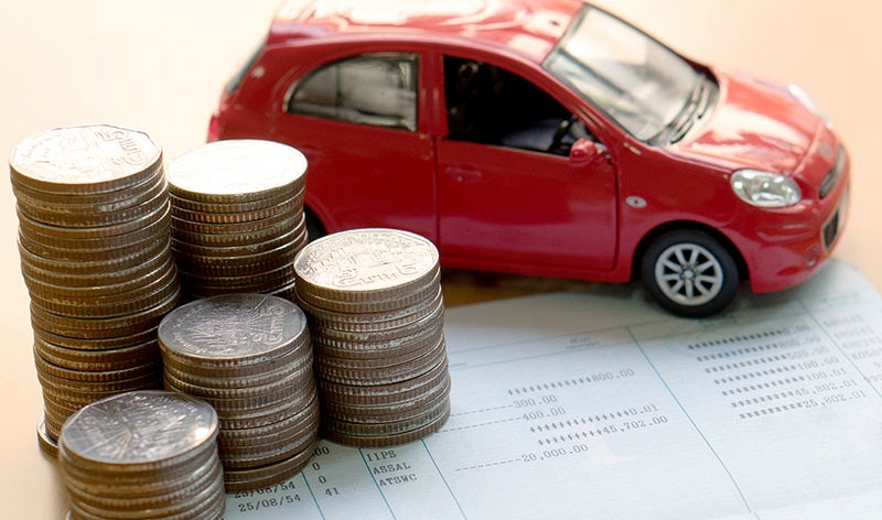 A red toy car sits behind stacks of coins on a document.