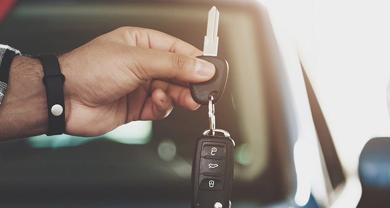 A hand holds car keys with a remote fob in front of a car interior.