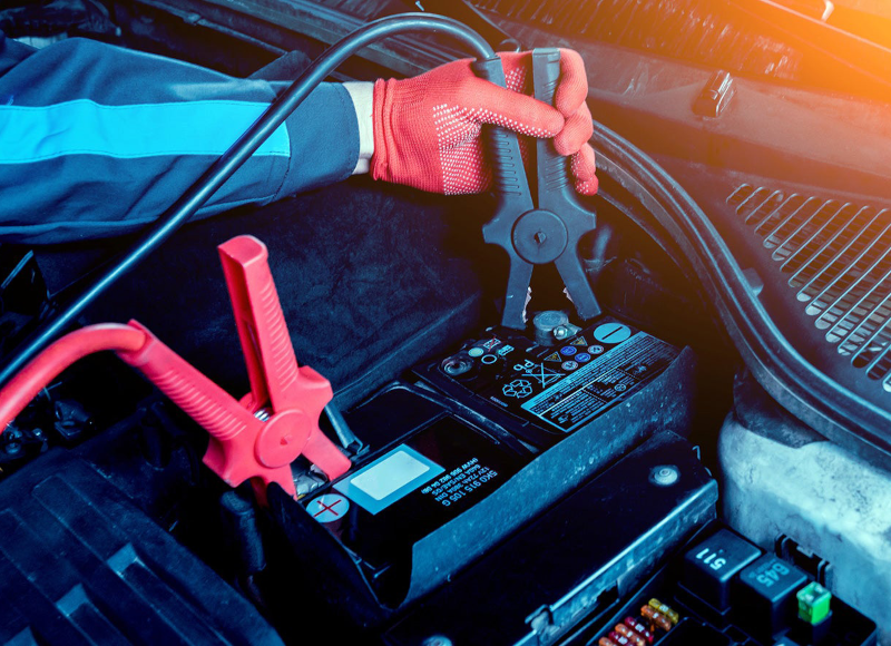 Mechanic in red gloves connecting jumper cables to a car battery terminal